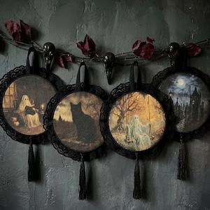 May include: Four circular wall hangings featuring gothic illustrations of a ghost reading, a black cat, a ghost on a swing, and a graveyard scene. Each piece is framed in black lace with a black tassel and suspended from a dark vine garland.