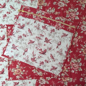 May include: Quilted fabric with a clear pocket, patterned with red birds and white flowers. The pocket has a gold zip. The background fabric is red with a floral design.