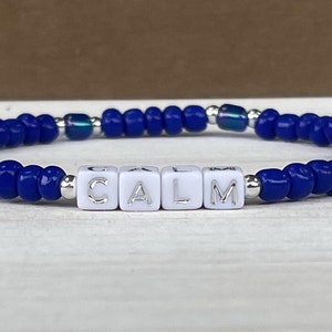 May include: Blue beaded bracelet with white letter beads spelling "CALM".