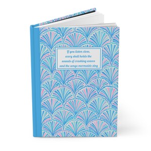 May include: A blue and white journal with a quote about seashells and mermaids. The cover features a repeating pattern of stylized seashells in shades of blue, pink, and white.