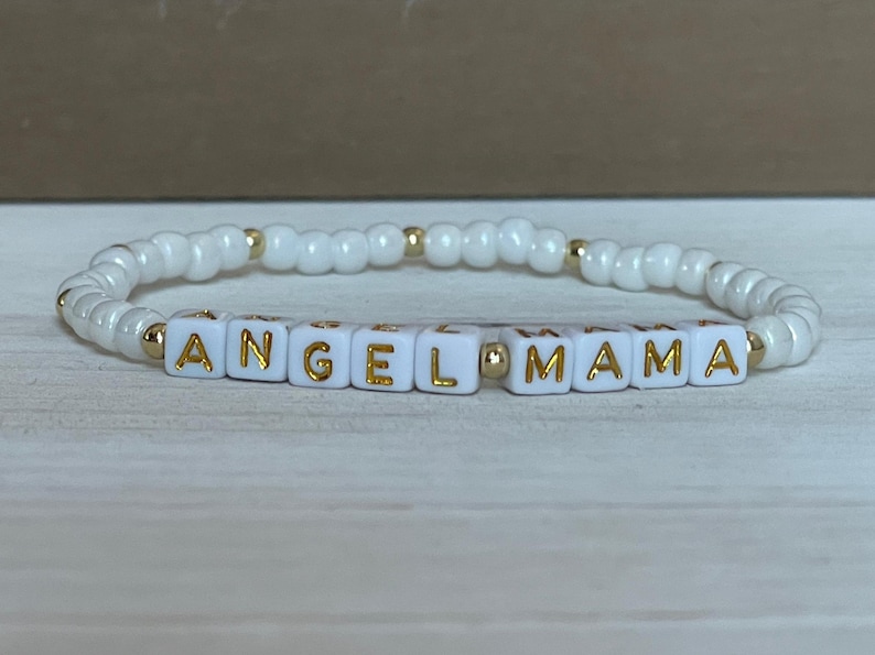 May include: White beaded bracelet with gold lettering spelling "ANGEL MAMA".