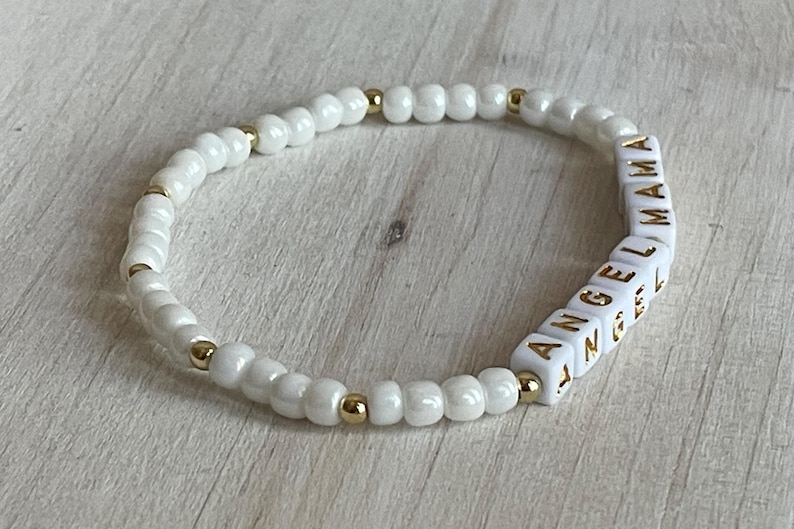 May include: White beaded bracelet with gold accents and white letter beads spelling "ANGEL MAMA".