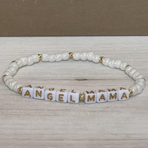 May include: White beaded bracelet with gold lettering spelling "Angel Mama".