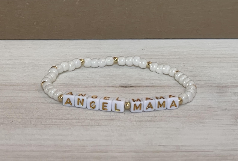 May include: White beaded bracelet with gold lettering spelling "Angel Mama".