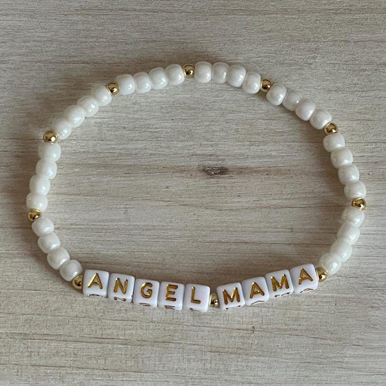 May include: White beaded bracelet with gold beads and the words "ANGEL MAMA" spelled out in gold letters on white square beads.