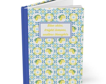 May include: A hardcover journal with a blue spine and a patterned cover featuring yellow lemons and blue floral designs. The journal has the text "Blue skies, bright lemons, endless thoughts" on the cover.