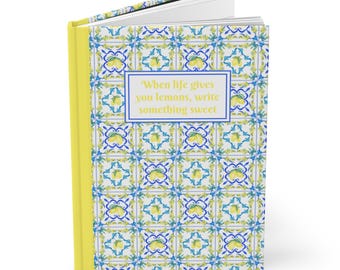 May include: A yellow-spined journal with a patterned cover featuring a lemon and floral design in blue, yellow, and white. The text "When life gives you lemons, write something sweet" is displayed on the cover.