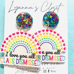 Op de afbeelding: Regenboogvormige oorringen in de vorm van een hart met de tekst "I love you all CLASS DISMISSED" en "e you all DISMISSED" op elke oorring. De oorringen zijn gemaakt van helder acryl met glittersterren aan de bovenkant.