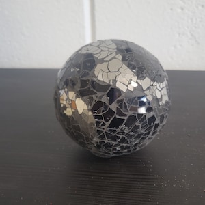 May include: A black and silver mosaic sphere ornament. The sphere is made of small, irregular pieces of glass that are arranged in a random pattern.