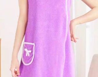 Può includere: Un telo da bagno avvolgente in spugna viola con bordi bianchi, scollo quadrato con due bottoni a pressione bianchi sulla parte superiore e una tasca applicata sul lato destro decorata con un piccolo fiocco bianco.