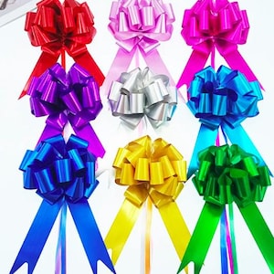 May include: A collection of nine decorative gift bows in a variety of vibrant colors including red, light pink, hot pink, purple, silver, light blue, dark blue, yellow, and green. Each bow features a full, rounded top and two long tails.