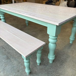 May include: A light wood-toned dining table and matching bench with mint green painted legs. The table has a rectangular top and turned legs. The bench has a similar design, offering a coordinated seating option. The table is approximately 72 inches long.