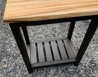 May include: A wooden table with a black painted frame and a natural wood top. The table has a shelf underneath.