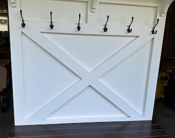 May include: White wooden entryway bench with a brown wood top and a shelf underneath. The bench has five black metal hooks on the back.