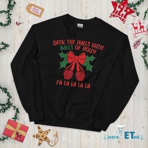 May include: Black Christmas sweater with a red bow and holly leaves. The text on the sweater reads "Deck the halls with balls of holly fa la la la la".