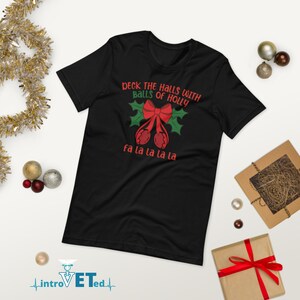 May include: Black t-shirt with a red and green Christmas design. The text reads "Deck the halls with balls of holly" and "fa la la la la".