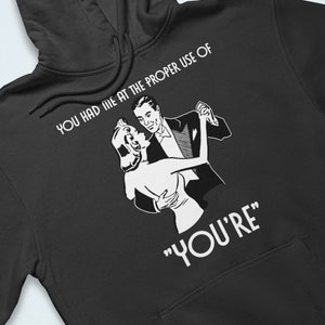 Peut inclure: Sweat-shirt à capuche noir avec un graphique blanc d'un couple dansant. Le texte sur le sweat-shirt est "You had me at the proper use of "You're" "
