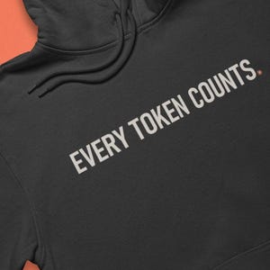 May include: A black hooded sweatshirt featuring a front kangaroo pocket and long sleeves. The chest area displays the text "EVERY TOKEN COUNTS." printed in a light grey, sans-serif font. The garment includes a matching drawstring hood.