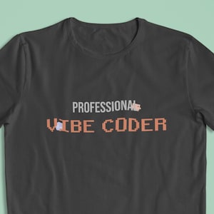 Könnte beinhalten: Dunkelgraues T-Shirt mit dem Text "PROFESSIONAL VIBE CODER" in orangefarbener Pixel-Schrift. Das T-Shirt hat einen Rundhalsausschnitt und kurze Ärmel. Der Hintergrund ist helltürkis.