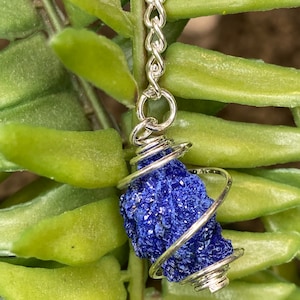 May include: A blue azurite crystal wrapped in silver wire, hanging from a silver chain. The crystal is a rough, natural shape and has a sparkly, iridescent finish.