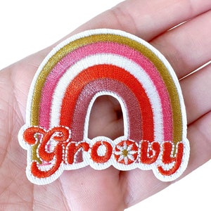 May include: Embroidered rainbow patch with gold, pink, orange, and red arches. The word "Groovy" is stitched in red with a gold outline and a flower detail. The patch is on a white background.