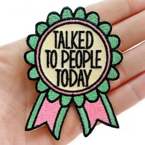 May include: Embroidered patch with the text "TALKED TO PEOPLE TODAY". The patch features a light beige center with black text, surrounded by a pink and green scalloped border and ribbons. The patch is a fun, wearable accessory.
