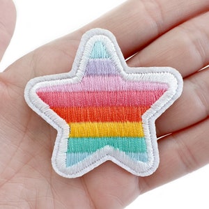 May include: A rainbow-colored star-shaped patch with a white outline. The star is made of fabric and has a stitched design.