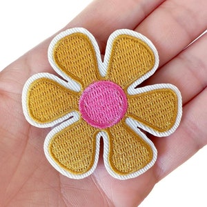 May include: A yellow flower patch with a pink center. The flower is embroidered with white stitching around the edges.