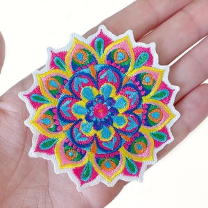 May include: A colorful embroidered mandala patch with a white border. The design features a symmetrical pattern with shades of pink, yellow, blue, and orange. This decorative patch can be used to embellish clothing or accessories.