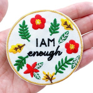 May include: White embroidered patch with a gold border. The patch features green leaves, red and yellow flowers, and the text "I AM enough".