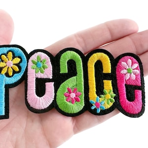 May include: A colorful embroidered patch with the word "Peace" in black outlined letters. Each letter is a different color and has a small flower design in the center.