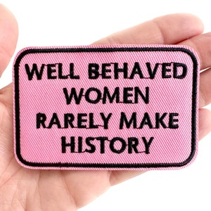 May include: Pink fabric patch with black embroidered text that reads "Well Behaved Women Rarely Make History."