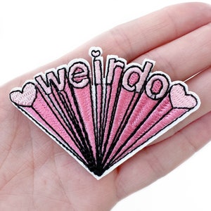 May include: Embroidered patch with the word "weirdo" in a pink, retro-style design. The patch features a radiating burst pattern with black outlines and heart accents, perfect for adding to clothing or accessories.