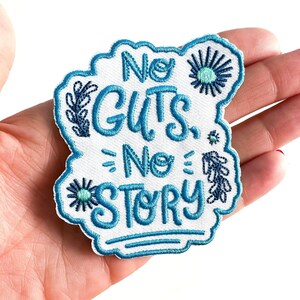 May include: White embroidered patch with blue stitching. The patch is shaped like a cloud and has the text "No Guts, No Story" in a blue cursive font. The patch is decorated with small blue flowers.