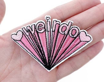 May include: Embroidered patch with the word "weirdo" in a pink, retro-style design. The patch features a radiating burst pattern with black outlines and heart accents, perfect for adding to clothing or accessories.