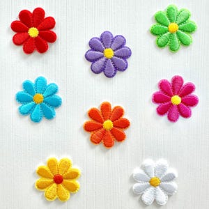 May include: A collection of embroidered daisy patches in various colors, including red, purple, blue, orange, pink, green, yellow, and white. Each patch features a yellow center and detailed stitching, perfect for crafting or embellishing clothing.