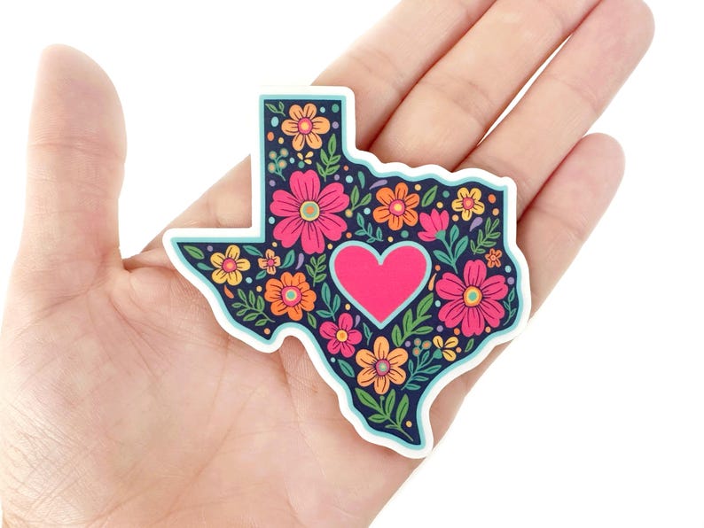May include: A sticker in the shape of Texas, filled with colorful flowers and a pink heart. The background is navy blue, and the flowers are pink, orange, and yellow. The sticker has a white border.