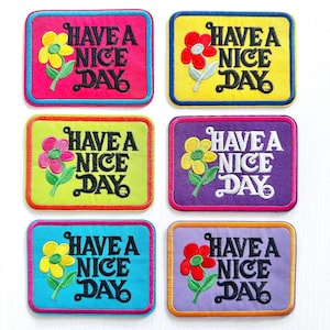 May include: Set of six embroidered patches with the phrase "Have a Nice Day" and a flower design. Each patch features a different color background, including pink, yellow, green, purple, and blue, with a contrasting border and flower color.