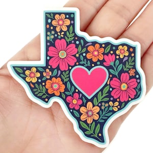 May include: A sticker in the shape of Texas, featuring a floral design. The sticker has a navy blue background with pink, orange, and yellow flowers, green leaves, and a pink heart in the center.