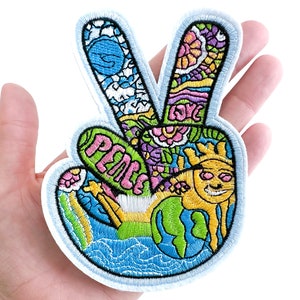 May include: A colorful peace sign patch with a peace symbol, flowers, a sun, and a globe. The patch is embroidered with a white outline and has a white background.