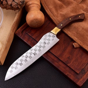 May include: A stainless steel kitchen knife with a checkered pattern on the blade and a brown wooden handle. The knife is on a wooden cutting board.