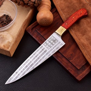May include: A stainless steel kitchen knife with a wood handle and a brass bolster. The blade has a Damascus pattern and an American flag design etched into it.