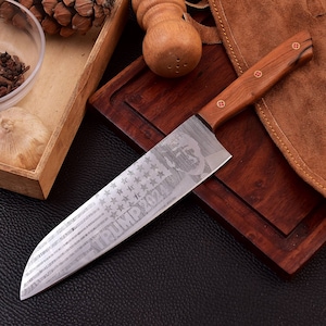 Peut inclure: Un couteau de cuisine en acier inoxydable avec un manche en bois. La lame est gravée d'un drapeau américain et du texte "TRUMP 2024".