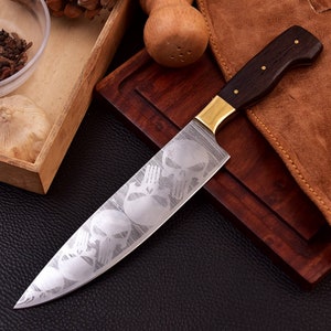 May include: A silver chef's knife with a black wooden handle and a brass bolster. The blade is etched with a repeating pattern of skulls.