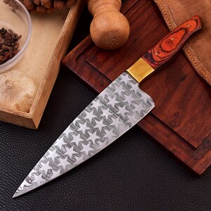 May include: A large chef's knife with a star-shaped pattern on the blade. The handle is made of wood with a red and brown finish. The knife is resting on a wooden cutting board.