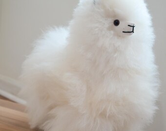 May include: A white fluffy alpaca plush toy. The toy is made of soft, white fur and has a cute, friendly face.