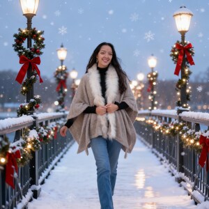 May include: A woman wearing a beige cape with a white fur collar and blue jeans walks on a snow-covered bridge. The bridge is decorated with Christmas lights and red bows. Snowflakes fall in the air, and the scene is illuminated by street lamps.