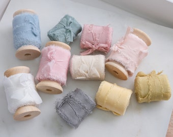 Puede incluir: Surtido de diez carretes de cinta de seda de colores con bordes deshilachados. Los carretes son de madera y tienen un acabado natural. Las cintas son de varios tonos de azul, rosa, amarillo y verde.