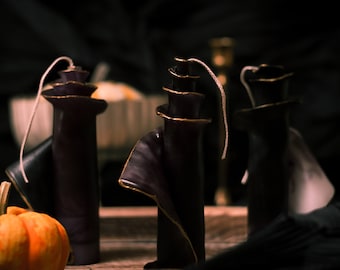 May include: Three black and gold candles with a spiral design. The candles are on a wooden surface with a small orange pumpkin in the foreground.