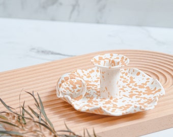 May include: White ceramic candle holder with a speckled gold design. The holder has a ruffled edge and a single candle cup.